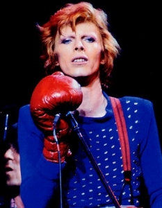 Дейвид Боуи
Глем рок иконата Дейвид Боуи (David Bowie) е знакова фигура в музиката през 70-те и 80-те години. Творчеството му се отличава с интелектуална задълбоченост и ексцентризъм, които изразява с визията си и с различния цвят на очите си, които всъщност са сини. При сбиване за момиче в ученическите си години, Боуи получава травма на едното си око, в резултат на което лещата му е винаги широко отворена. Различният цвят на очите е измама и част от атрактивния му имидж.